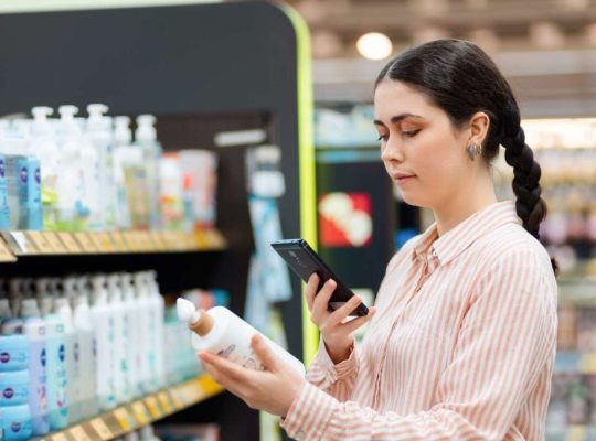Young Woman Holding Smartphone and Scanning Qr Code on Bottle of Cosmetics